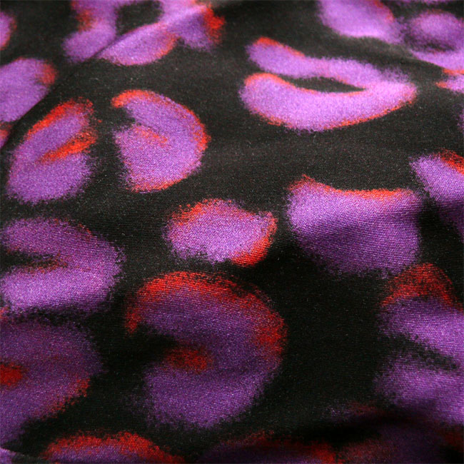 gros plan d'un tissu noir imprimé motifs panthère stylisés (des C assez épais) violets soulignés par ci par là d'un orange électrique