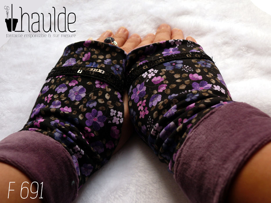 Paire de mitaines en jersey noir imprimé petites fleurs violettes. Un galon de deux rangs de sequins noirs décore au niveau des phalanges. Manchettes en velours mauve Vue de la paire portée