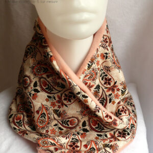 Cache col croisé, le côté droit replié sur le gauche. Dessus en jersey blanc imprimé paisley et fleurs dans les tons roses et marrons. Dessous en polaire de coton rose pâle un peu orangé. Vu de face sur une tête de mannequin