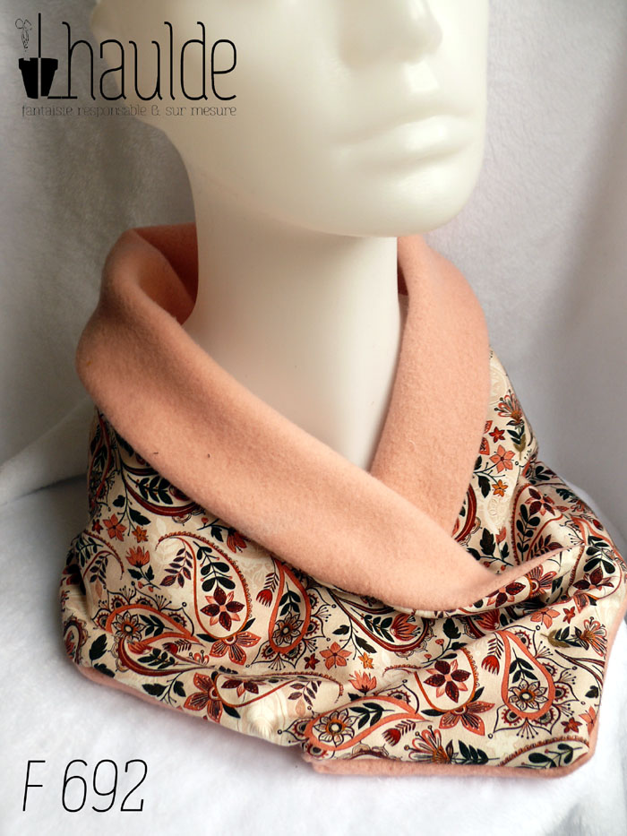 Cache col croisé, le côté droit replié sur le gauche. Dessus en jersey blanc imprimé paisley et fleurs dans les tons roses et marrons. Dessous en polaire de coton rose pâle un peu orangé. Vu avec la polaire repliée sur le jersey, comme un col châle, de trois quarts sur une tête de mannequin
