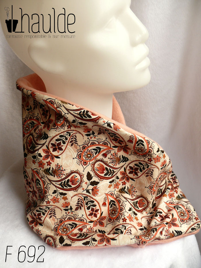 Cache col croisé, le côté droit replié sur le gauche. Dessus en jersey blanc imprimé paisley et fleurs dans les tons roses et marrons. Dessous en polaire de coton rose pâle un peu orangé. Vu de profil sur une tête de mannequin