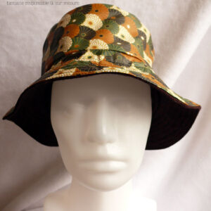 Bob en toile enduite imprimé de chrysanthèmes stylisés disposés en queue de paon, kaki, noir, ocre et blanc dans un style japonais L'autre face du bob est en laine Vu sur une tête de mannequin