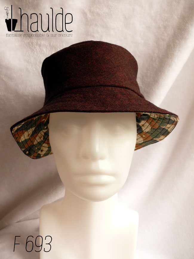 Bob en toile enduite imprimé de chrysanthèmes stylisés disposés en queue de paon, kaki, noir, ocre et blanc dans un style japonais L'autre face du bob est en laine Vu côté laine noir-rouge de face sur une tête de mannequin. Sous le rebord la toile enduite est visible