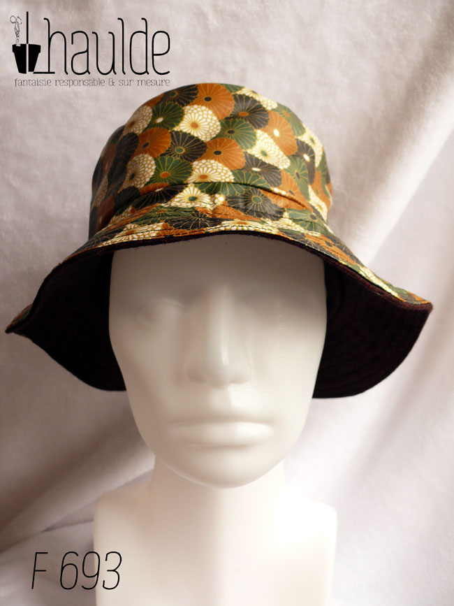 Bob en toile enduite imprimé de chrysanthèmes stylisés disposés en queue de paon, kaki, noir, ocre et blanc dans un style japonais L'autre face du bob est en laine Vu sur une tête de mannequin