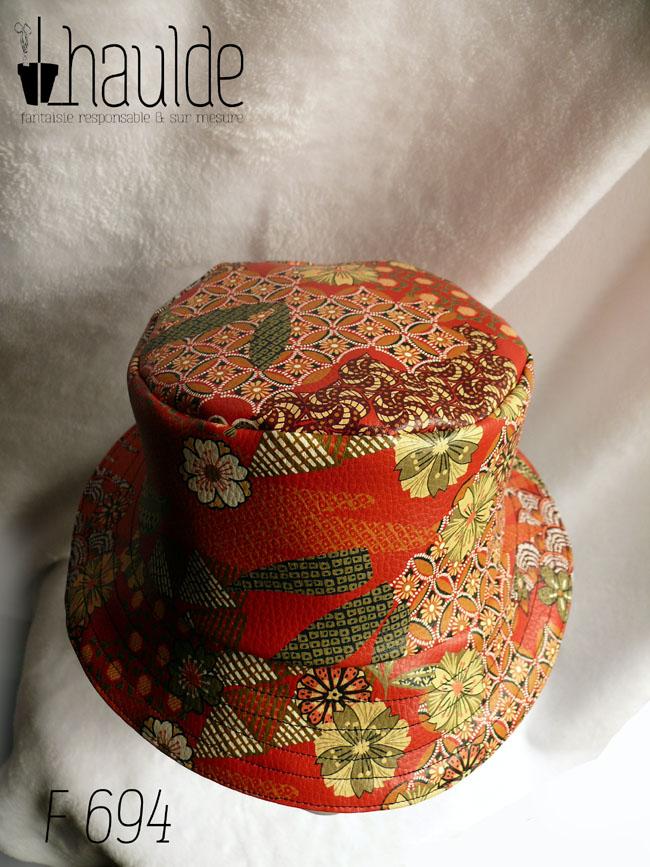 Bob en simili cuir rouge imprimé motifs floraux d'esthétique japonaise dans les tons kakis, jaune pâle et orange, cernés de noir. L'autre face du bob est en velours milleraies noir Vu de dessus