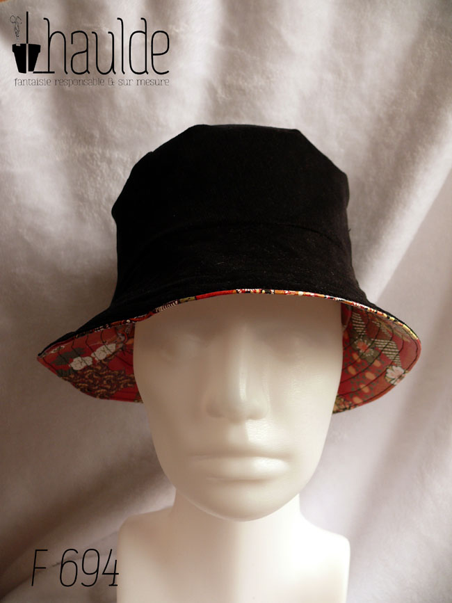 Bob en simili cuir rouge imprimé motifs floraux d'esthétique japonaise dans les tons kakis, jaune pâle et orange, cernés de noir. L'autre face du bob est en velours milleraies noir Vu côté milleraies noir de face sur une tête de mannequin, sous le rebord le simili cuir apparait