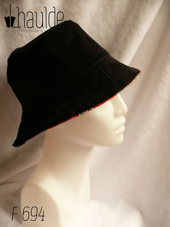 Bob en simili cuir rouge imprimé motifs floraux d'esthétique japonaise dans les tons kakis, jaune pâle et orange, cernés de noir. L'autre face du bob est en velours milleraies noir Vu côté milleraies noir de profil sur une tête de mannequin