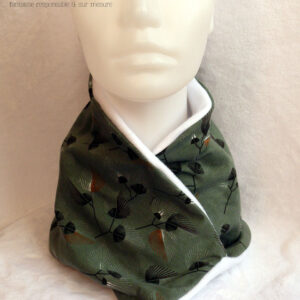 Tour de cou croisé en jersey fond vert céladon imprimé fleurs stylisées façon plumeaux, noir blanc et orange foncé, doublé de polaire blanche Vu porté de face sur une tête de mannequin