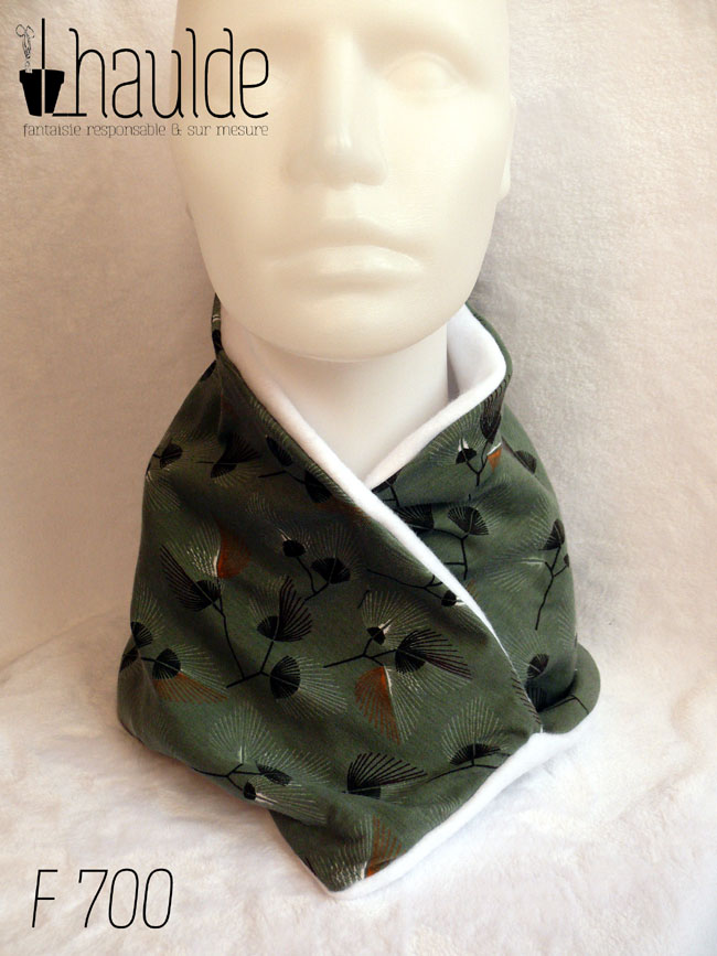 Tour de cou croisé en jersey fond vert céladon imprimé fleurs stylisées façon plumeaux, noir blanc et orange foncé, doublé de polaire blanche Vu porté de face sur une tête de mannequin