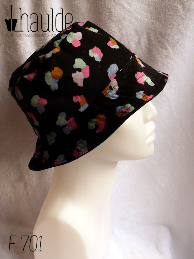 Bob en milleraies noir imprimé de taches regroupées par trois ou quatre, mauve, vert pâle, ocre, rose et bleu, qui pourraient faire penser à un pelage animal (le motif s'appelle animal skin) Réversible sur du sergé noir uni Vu de profil sur une tête de mannequin