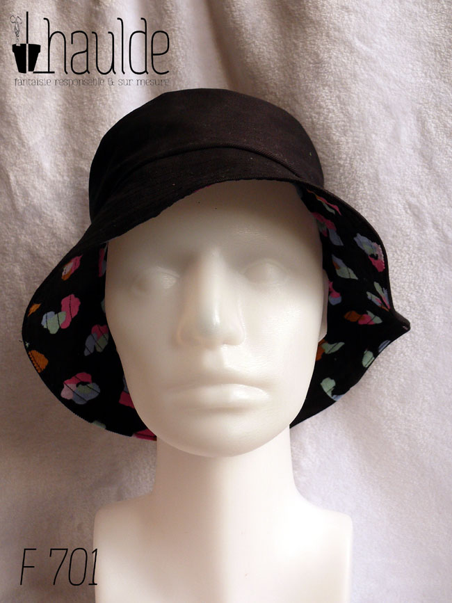 Bob en milleraies noir imprimé de taches regroupées par trois ou quatre, mauve, vert pâle, ocre, rose et bleu, qui pourraient faire penser à un pelage animal (le motif s'appelle animal skin) Réversible sur du sergé noir uni Vu de face côté sergé, sous le rebord la face imprimée se voit