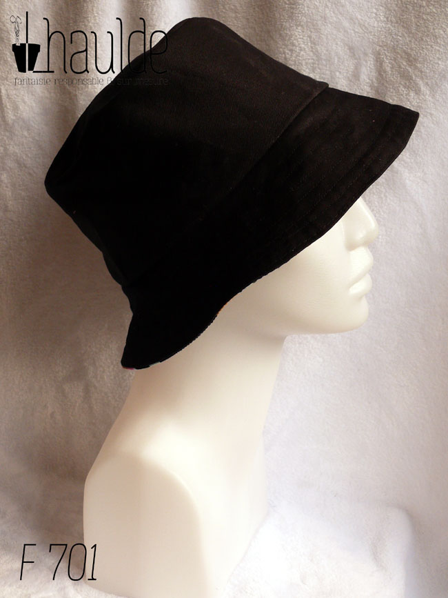 Bob en milleraies noir imprimé de taches regroupées par trois ou quatre, mauve, vert pâle, ocre, rose et bleu, qui pourraient faire penser à un pelage animal (le motif s'appelle animal skin) Réversible sur du sergé noir uni Vu de profil côté sergé, porté par une tête de mannequin