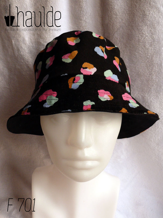 Bob en milleraies noir imprimé de taches regroupées par trois ou quatre, mauve, vert pâle, ocre, rose et bleu, qui pourraient faire penser à un pelage animal (le motif s'appelle animal skin) Réversible sur du sergé noir uni Vu de dessus côté milleraies, porté par une tête de mannequin