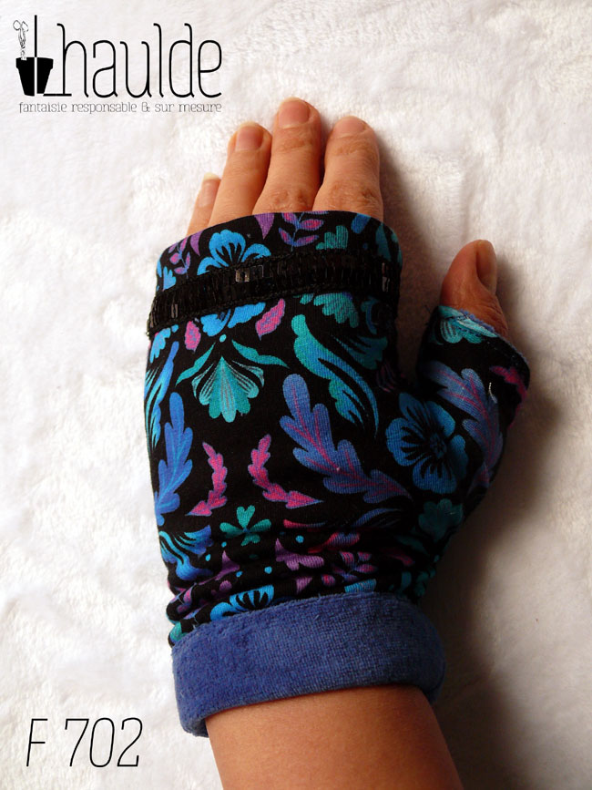 Paire de mitaines avec pouce long en jersey noir imprimé motifs végétaux stylisés et symétriques dans les tons bleus électriques, turquoise, fuchsia et mauve Le haut de la mitaine est traversé par un galon de deux rangs de sequins carrés noirs. La manchette est en velours bleu roi Vue de dessus, porté