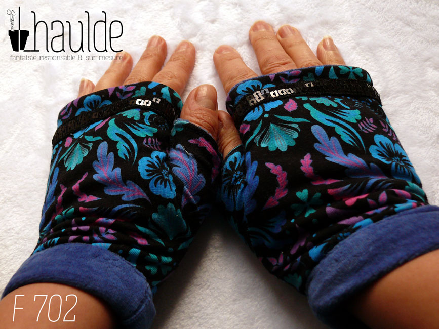 Paire de mitaines avec pouce long en jersey noir imprimé motifs végétaux stylisés et symétriques dans les tons bleus électriques, turquoise, fuchsia et mauve Le haut de la mitaine est traversé par un galon de deux rangs de sequins carrés noirs. La manchette est en velours bleu roi Vue de la paire, portée