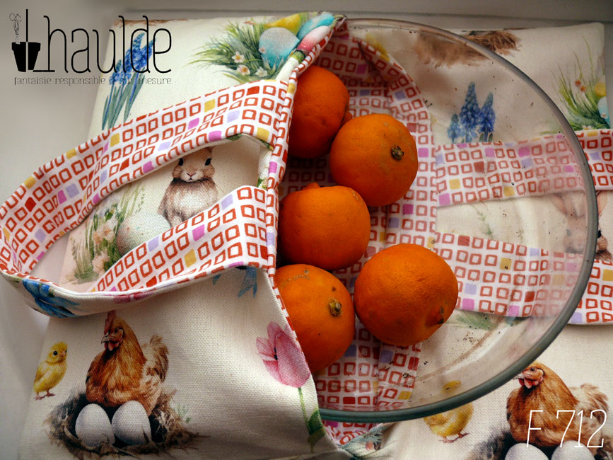 Sac à tarte, le dessus est en toile blanche imprimée de petits lapins, poules couveuses, poussins, petit agneau endormis, fleurs variées, et nids d'oeufs de Pâques dans un style illustration jeunesse à l'aquarelle. L'intérieur est en tissus spécial contact alimentaire blanc imprimé de carrés oranges à intérieur blanc alignés avec de temps en temps un carré plein mauve, rose, jaune ou orange Le sac est vu de dessus, entrouvert avec un plat à manqué en pyrex qui sort, il est rempli de citrons bergamotes