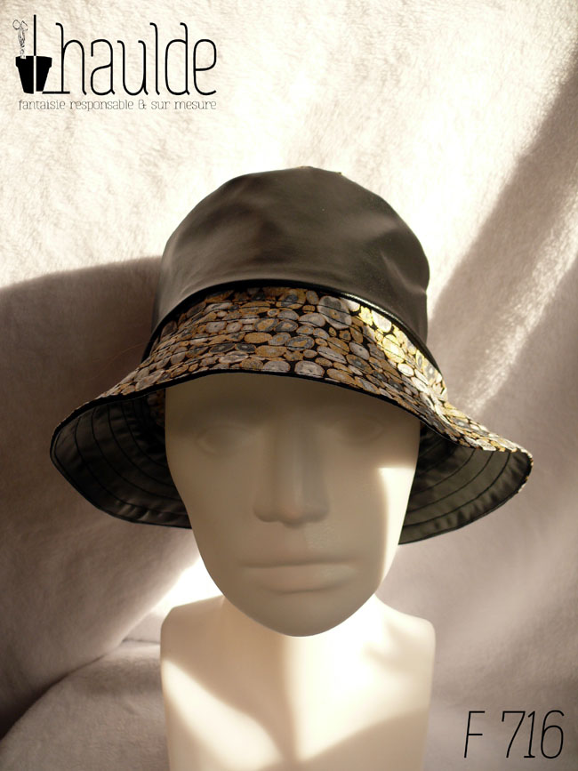 Bob en simili cuir noir et tissu imprimé. Les motifs sont des ovales concentriques de petite taille inspirés par Klimt dans les tons gris rehaussés de doré. Ici le dessus du bob est en imprimé, la bande centrale en uni, le bord en imprimé Vu de face sur une tête de mannequin