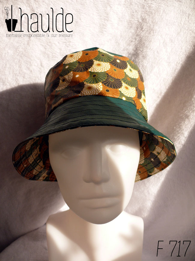 Bob en simili cuir vert et toile enduite imprimée de fleurs stylisées de type chrysanthèmes alignées les unes sur les autres comme un motif queue de paon. Elles sont blanches ou marron roux, ou noires ou vertes. Ici le dessus du bob est en simili uni, la bande centrale en imprimé, le bord en uni Vu de face sur une tête de mannequin