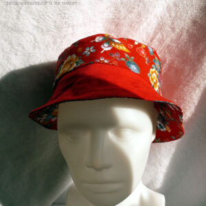 Bob court en tissu rouge imprimé pivoines, papillons et autres fleurs multicolores soulignées de doré, d'inspiration Est asiatique (Chine ou Japon) et sergé rouge, réversible. Ici le dessus est en tissu uni, la bande centrale en imprimé, le bord en uni vu de face sur une tête de mannequin