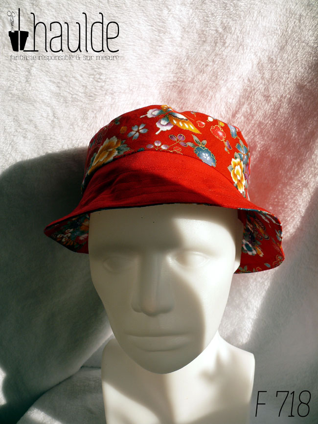 Bob court en tissu rouge imprimé pivoines, papillons et autres fleurs multicolores soulignées de doré, d'inspiration Est asiatique (Chine ou Japon) et sergé rouge, réversible. Ici le dessus est en tissu uni, la bande centrale en imprimé, le bord en uni vu de face sur une tête de mannequin