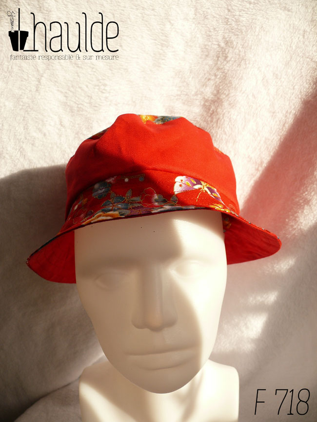 Bob court en tissu rouge imprimé pivoines, papillons et autres fleurs multicolores soulignées de doré, d'inspiration Est asiatique (Chine ou Japon) et sergé rouge, réversible. Ici le dessus est en tissu imprimé, la bande centrale en rouge uni, le bord en imprimé vu de face sur une tête de mannequin