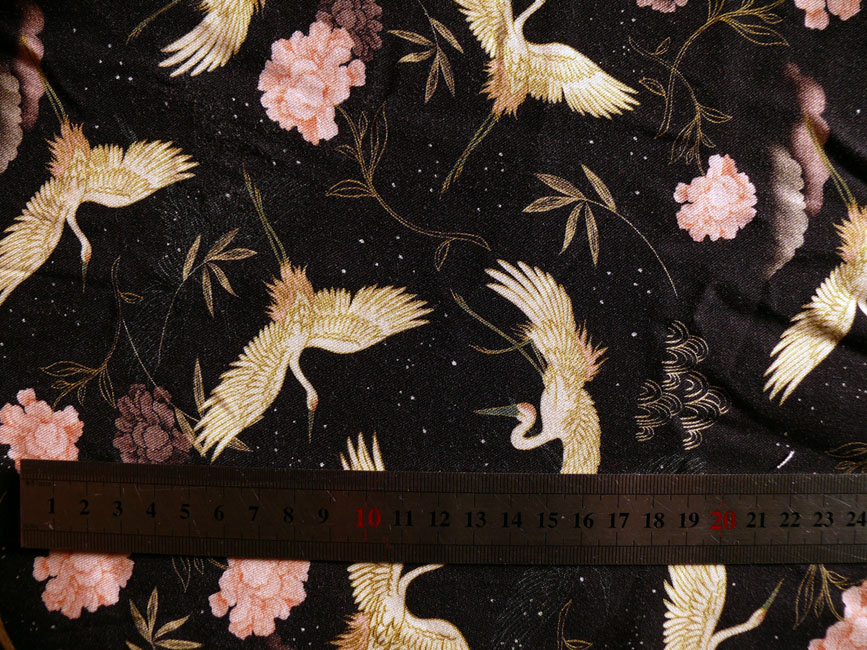 tissu léger et souple noir imprimé grues blanches et fleurs délicates (ressemblant un peu à des oeillets) rose pâle. L'ensemble est gracieux Le mètre posé dessus indique que les grues ailes déployées font 7 cm d'envergure, les fleurs 3 cm de large max