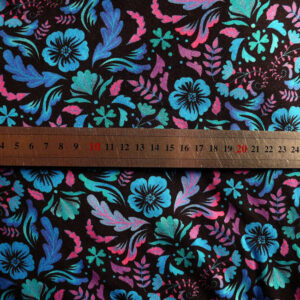jersey noir imprimé fleurs et végétaux stylisés répartis de manière symétriques, dans les tons bleus fluo, vert émeraude fluo, rose et mauve fluo Le mètre posé dessus indique que les fleurs font 2.5 cm de large max, les feuilles sont longues de 4 cm max