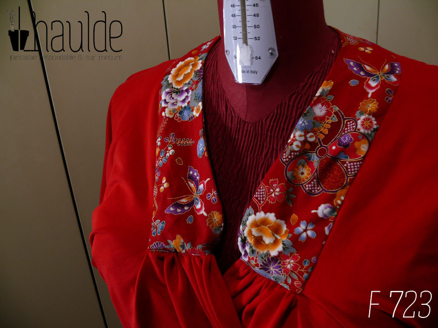 Vue de détail du col Haut coeur croisé à manches courtes en jersey rouge qui blouse jusqu'à la taille et jersey noir moulant de la taille aux hanches Le col est garni de tissu rouge imprimé fleurs et papillons d'inspiration Est asiatique, soulignés de doré. Vu sur un mannequin de couture réglé en taille 52