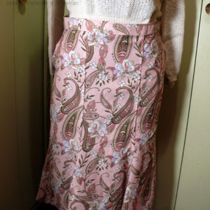 Jupe mi longue à quilles (pans supplémentaires en bas, qui froufroutent quand on marche) en sergé de viscose rose pâle imprimé paisley et fleurs dans les tons roses et gris, soulignés de vert foncé, rehaussés de blanc. Vue de face sur un mannequin de couture réglé en 44 La ceinture est un peu large.