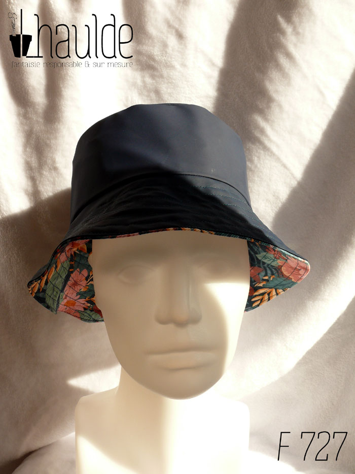 Bob en toile imperméable bleu marine réversible sur de la gabardine imprimée de motifs feuillage vert pastel et fleurs roses sur fond bleu marine. On aperçoit le tissu imprimé sous le bord Vu de face sur une tête de mannequin