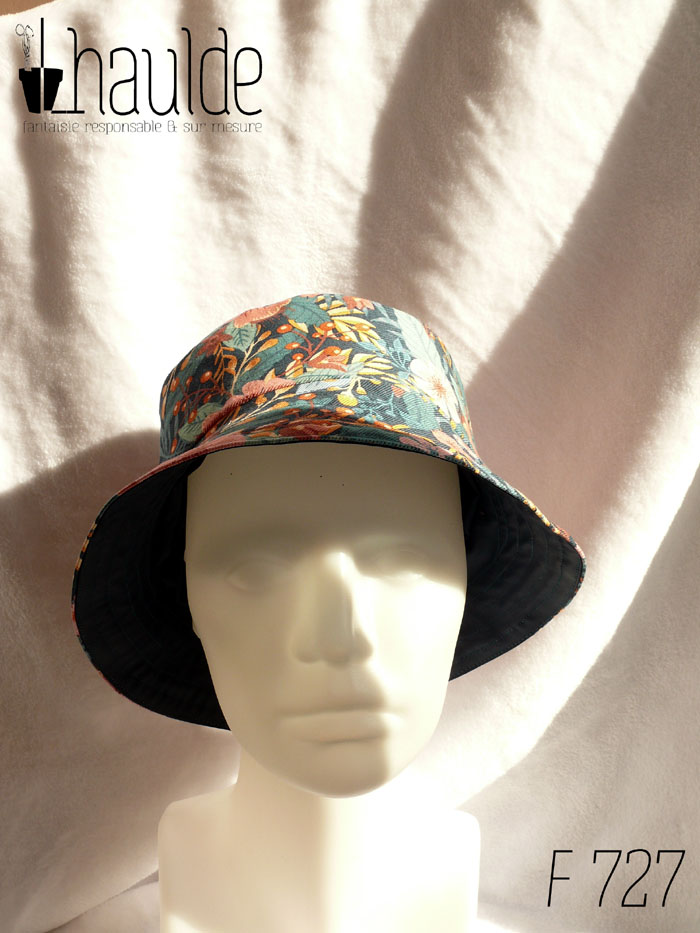 Bob en gabardine imprimée de motifs feuillage vert pastel et fleurs roses sur fond bleu marine. Vue de face sur une tête de mannequin. On aperçoit au niveau du bord l'envers en toile imperméable bleu marine