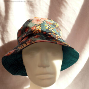 Bob en gabardine imprimée de motifs feuillage vert pastel et fleurs roses sur fond bleu marine. Vue de face sur une tête de mannequin. On aperçoit au niveau du bord l'envers en sergé vert pétrole