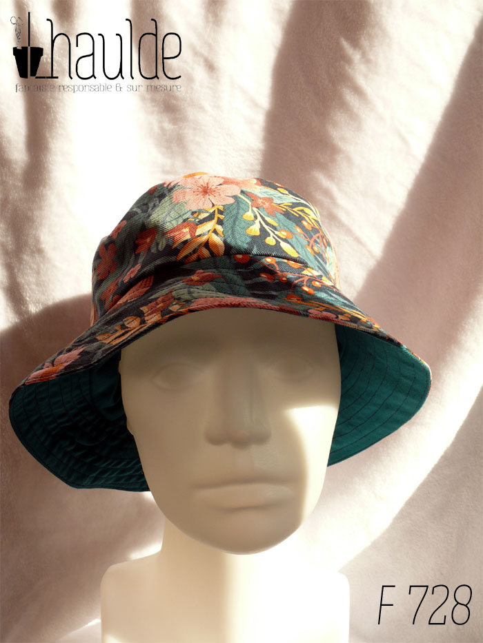 Bob en gabardine imprimée de motifs feuillage vert pastel et fleurs roses sur fond bleu marine. Vue de face sur une tête de mannequin. On aperçoit au niveau du bord l'envers en sergé vert pétrole