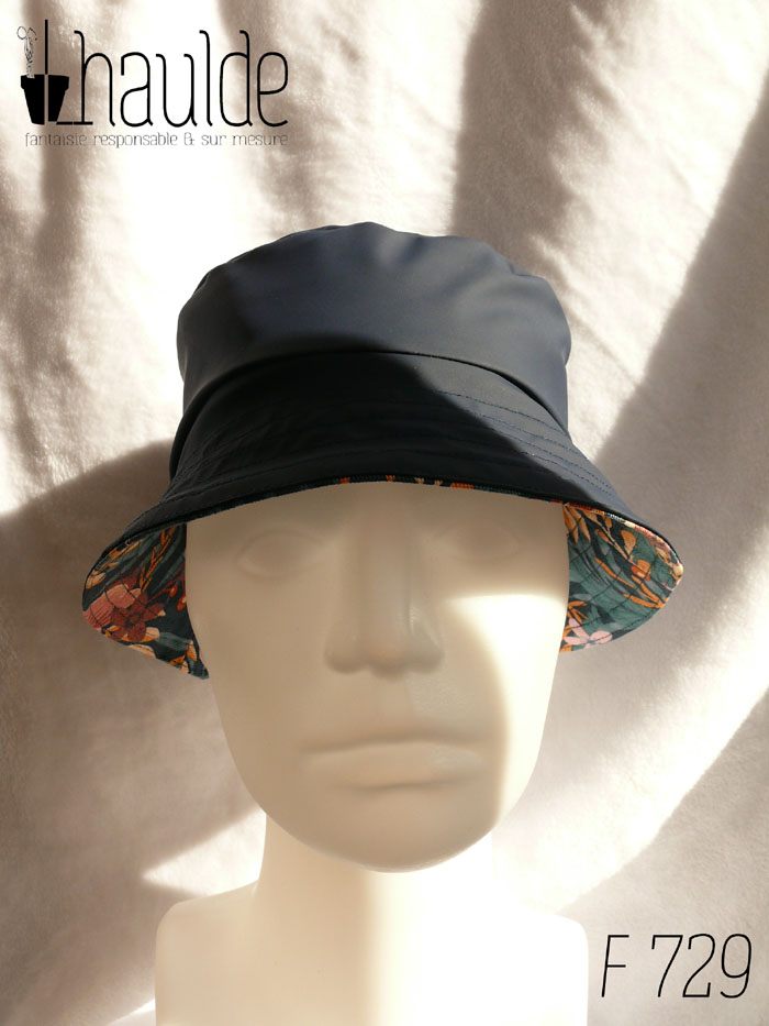 Bob court en toile imperméable bleu marine réversible sur de la gabardine imprimée de motifs feuillage vert pastel et fleurs roses sur fond bleu marine. On aperçoit le tissu imprimé sous le bord Vu de face sur une tête de mannequin