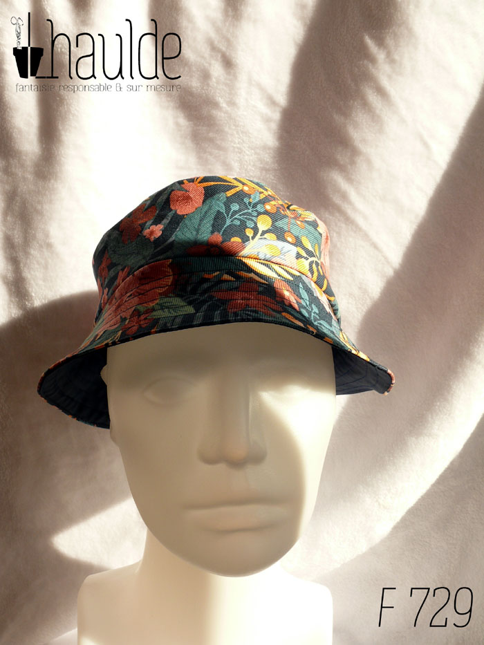 Bob court en gabardine imprimée de motifs feuillage vert pastel et fleurs roses sur fond bleu marine. Vue de face sur une tête de mannequin. On aperçoit au niveau du bord l'envers en toile imperméable bleu marine