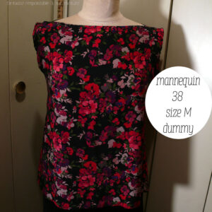 Haut sans manches en viscose noire imprimée de fleurs rouges vif tirant sur le rose et de fleurs plus foncées dans les tons violets et plus claires dans les tons mauves, le tout rehaussé de petites feuilles kaki foncé Col bateau, coupe très évasée Vue de face sur un mannequin de couture réglé en taille 38/M