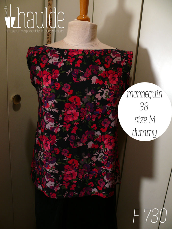 Haut sans manches en viscose noire imprimée de fleurs rouges vif tirant sur le rose et de fleurs plus foncées dans les tons violets et plus claires dans les tons mauves, le tout rehaussé de petites feuilles kaki foncé Col bateau, coupe très évasée Vue de face sur un mannequin de couture réglé en taille 38/M