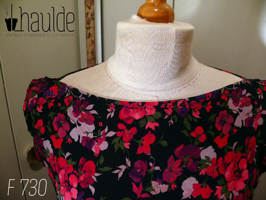 Haut sans manches en viscose noire imprimée de fleurs rouges vif tirant sur le rose et de fleurs plus foncées dans les tons violets et plus claires dans les tons mauves, le tout rehaussé de petites feuilles kaki foncé Col bateau, coupe très évasée Vue de détail de l'encolure sur un mannequin de couture réglé en taille 38/M