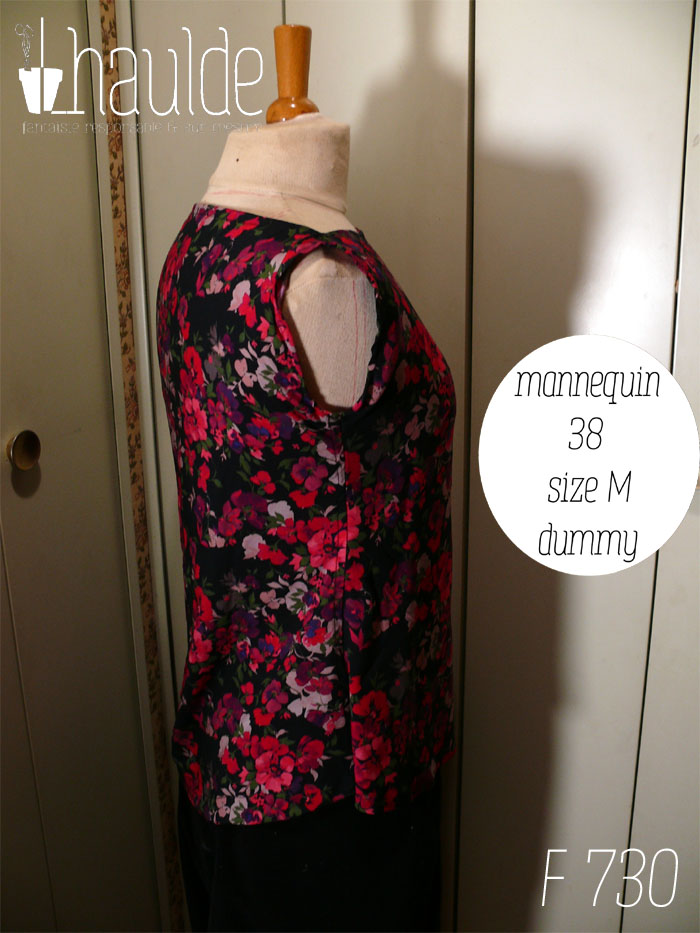 Haut sans manches en viscose noire imprimée de fleurs rouges vif tirant sur le rose et de fleurs plus foncées dans les tons violets et plus claires dans les tons mauves, le tout rehaussé de petites feuilles kaki foncé Col bateau, coupe très évasée Vue de profil sur un mannequin de couture réglé en taille 38/M Les emmanchures sont étroites