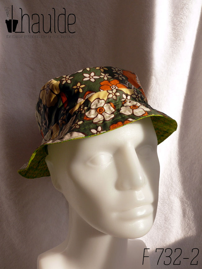 Bob court réversible, vu du côté en toile enduite, fond kaki imprimé de grandes fleurs oranges et jaune pâle dans le style des années 70. Vu de face sur une tête de mannequin