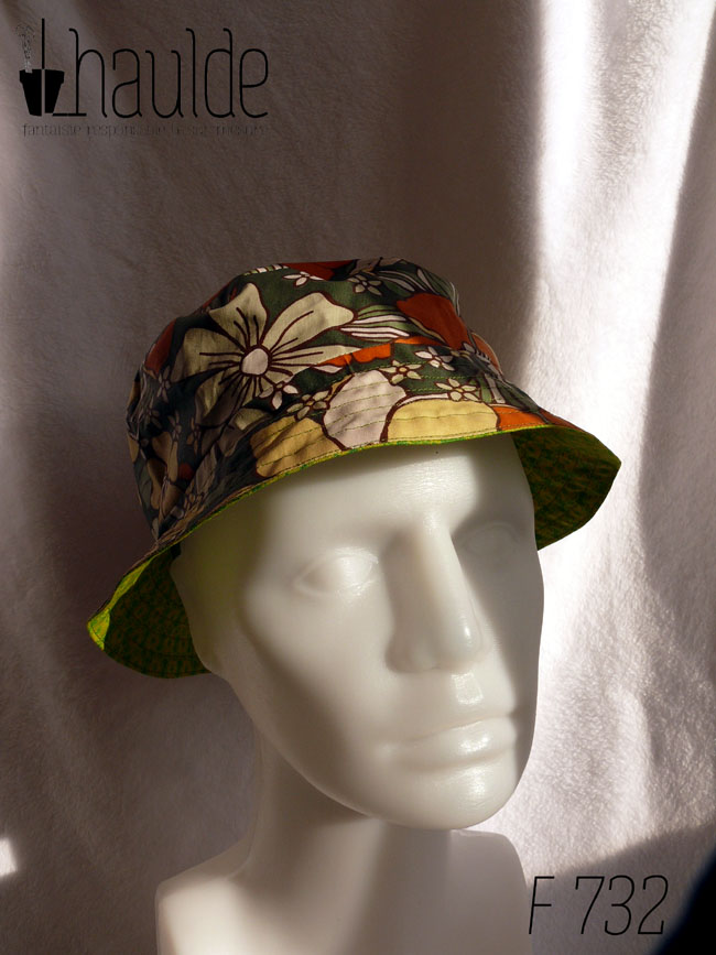 Bob court réversible, vu du côté en toile enduite, fond kaki imprimé de grandes fleurs oranges et jaune pâle dans le style des années 70. Vu de face sur une tête de mannequin