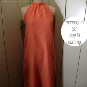 Robe mi longue dos nu nouée autour du cou, sans décolleté, en double gaze corail clair un peu orangé. Vue de face sur un mannequin de couture réglé en taille 38/M