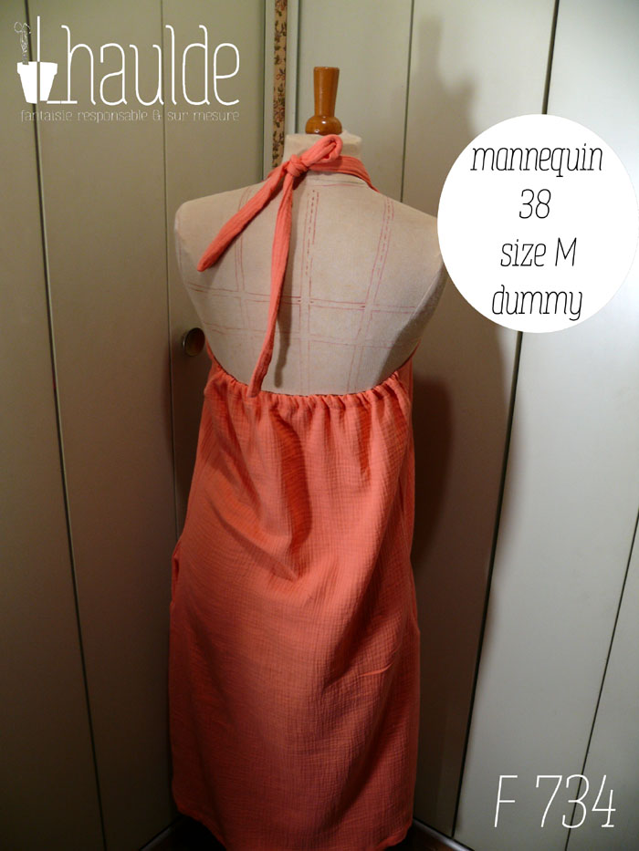 Robe mi longue dos nu nouée autour du cou, sans décolleté, en double gaze corail clair un peu orangé. Le bas du dos nu est élastiqué, il arrive un peu au-dessus de la taille Vue de dos sur un mannequin de couture réglé en taille 38/M