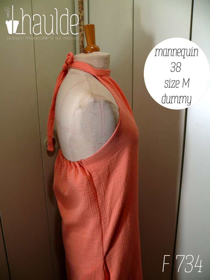 Robe mi longue dos nu nouée autour du cou, sans décolleté, en double gaze corail clair un peu orangé. Vue de profil sur un mannequin de couture réglé en taille 38/M Le dos est élastiqué, mon mannequin manque cruellement de muscles glutéaux