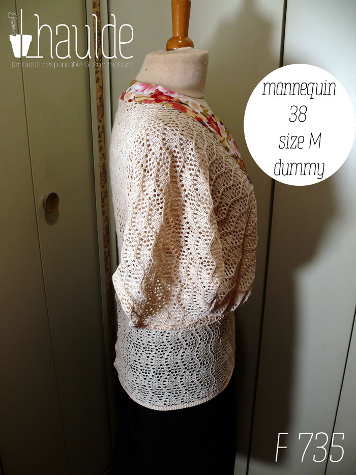 Haut manches mi longues en tricot de coton écru très ajouré, façon crochet, à motifs queues de paons en lignes horizontales. Le col plat est en tissu imprimé, fond doré avec de grosses fleurs de cerisier rouges, blanches et roses, soulignées de vrai doré. Le haut est ample et froncé jusqu'au hanches qu'il moule. Les manches descendent jusqu'au niveau du coude dessus, mais sont plus courtes dessous Vu de profil sur un mannequin de couture réglé en taille 38/M