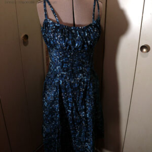 Robe mi-longue avec deux paires de fines bretelles réglables, buste plissé, taille ajustée, jupe ample, en popeline bleu nuit imprimé petite fleurs et végétaux délicats en dégradé de bleu jean Vue de face sur un mannequin de couture