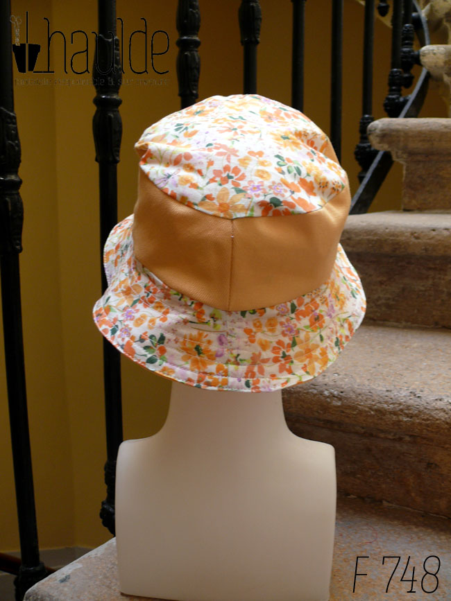 Bob court en sergé jaune pâle et tissu blanc imprimé de fleurs oranges et roses Bord fleurs, bande centrale jaune, sommet fleurs, vu de dos sur une tête de mannequin Sur l'envers les bandes sont inversées
