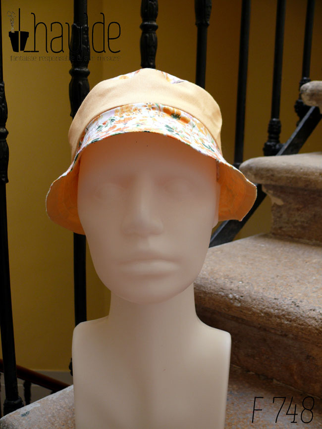 Bob court en sergé jaune pâle et tissu blanc imprimé de fleurs oranges et roses Bord fleurs, bande centrale jaune, sommet fleurs, vu de face sur une tête de mannequin Sur l'envers les bandes sont inversées