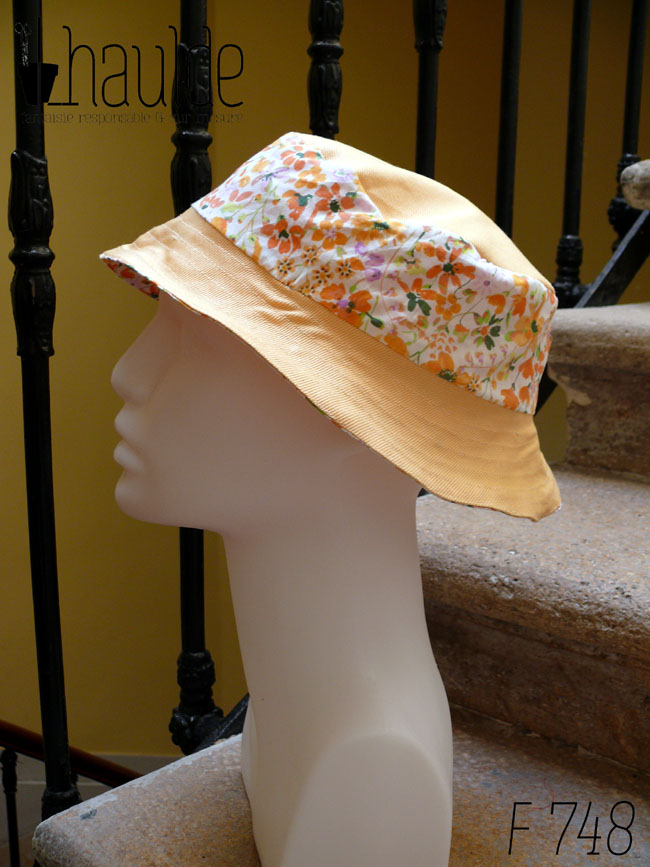 Bob court en sergé jaune pâle et tissu blanc imprimé de fleurs oranges et roses Bord jaune, bande centrale fleurs, sommet jaune, vu de profil sur une tête de mannequin Sur l'envers les bandes sont inversées