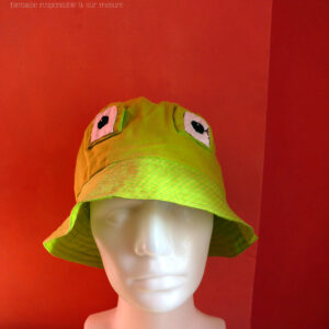 Bob grenouille avec des yeux en tissu cousus dessus. Le haut du bob est en tissu vert anis, le rebord dans un tissu un peu plus clair vert acide avec des lignes de losanges un peu plus foncées Vu de face sur une tête de mannequin